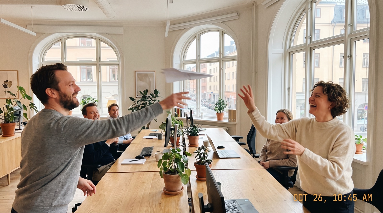 Ein Team im Büro: Ein Mann wirft einer lachenden Kollegin einen Papierflieger zu